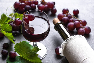 Wall Mural - Glass of wine with red grapes and wine bottle on dark background