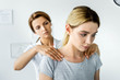 © LIGHTFIELD STUDIOS - selective focus of chiropractor touching shoulders of attractive patient in grey t-shirt