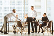 © xartproduction - A team of young businessmen working and communicating together in an office. Corporate businessteam and manager in a meeting. desktop against the background of the pan window, free space for text
