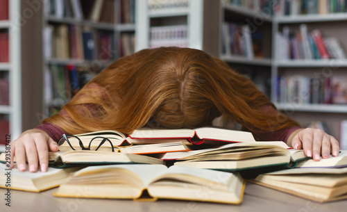 Fotomural Tired redhead girl sleeping on books at campus library