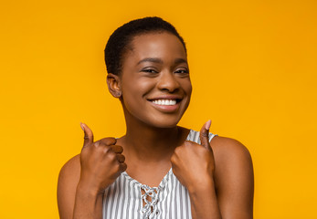 Wall Mural - Overjoyed afro girl showing thumbs up on yellow background