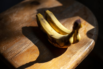 Bananas lie on a wooden surface. Two bananas in natural light. Fruits lie on a chair.