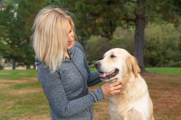 A girl in sportswear caresses a golden retriever dog and looks with care. In a coniferous forest against a background of trees, grass and fallen needles