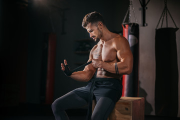 Brutal guy in the gym class concentrated wraps his hands with a professional bandages in front of the camera preparing for training