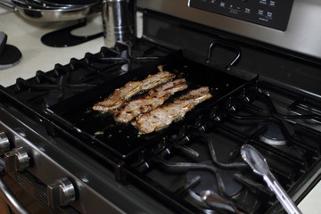 Wall Mural - Korean style BBQ short ribs, known as Kalbi, on a carbon steel griddle in a home kitchen.