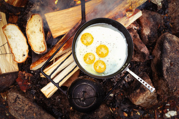 Eggs in small frying pan on bonfire. Camping in the forest. 