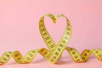 Yellow measuring tape in the shape of a heart on a pink background. The concept of weight loss for the normal functioning of the heart and body