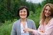 Outdoors portrait of senior mother and adult daughter are communicating outside over landscape of forest and mountains. Two generations concept