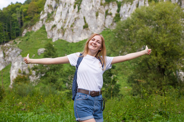 Young woman with backpack giving thumbs up. Trekking and tourism concept. Copyspace. A young pretty girl standing on a background of mountains