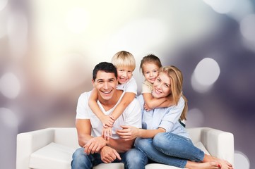 Wall Mural - Loving parents with their little son and daughter posing together for a portrait leaning over the back of a large sofa in the living room