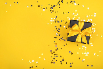 Wall Mural - Gift box on yellow background with sparkling confetti.