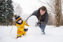 Little Boy With His Father Building Snowman In Snowy Park. Active Outdoors Leisure With Children In Winter.