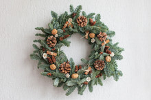 Christmas Wreath Made Of Natural Fir Branches  Hanging On A White Wall.  Wreath With Natural Ornaments: Bumps, Walnuts, Cinnamon, Cones. New Year And Winter Holidays. Christmas Decor