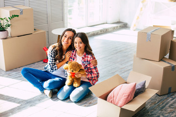 Wall Mural - My sweetie. Cheerful friendly mother and daughter are hugging while sitting on the floor in their new house, surrounded by boxes.