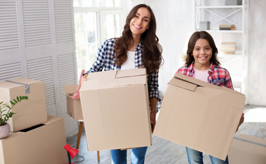 Wall Mural - We can do everything. Brunette adult mother and a smiley little girl are holding cardboard boxes in their new placement.