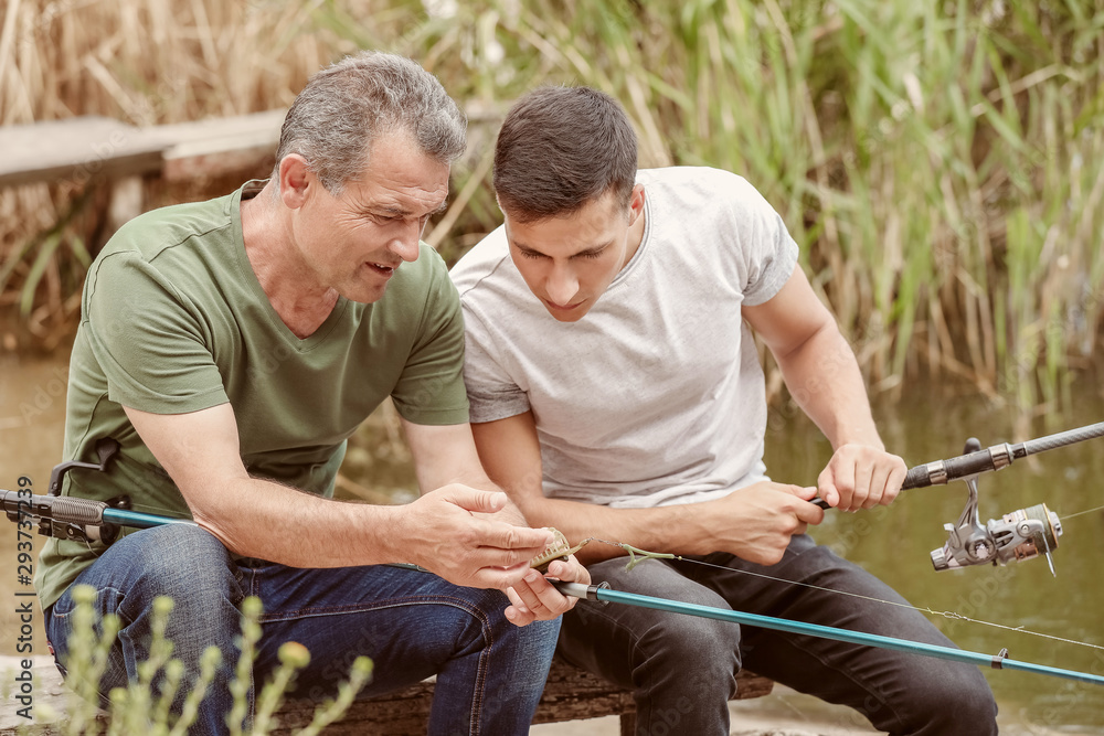 Young man and his father fishing on river