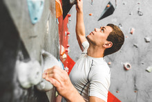 Sportsman Climber Moving Up On Steep Rock, Climbing On Artificial Wall Indoors. Extreme Sports And Bouldering Concept