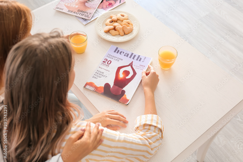 Mother and daughter with magazine at kitchen table