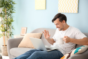 Handsome man with laptop drinking coffee at home