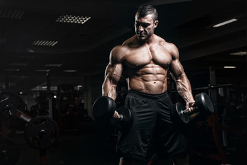 Wall Mural - Muscular athletic bodybuilder fitness model training arms with dumbbells in gym. Concept sport photo of exercises in gym
