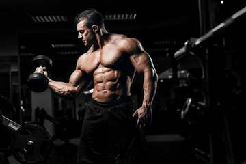 muscular athletic bodybuilder fitness model training arms with dumbbells in gym. concept sport photo