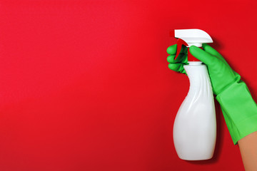 Worker's hand in a rubber green protective glove with a spray bottle on a red color background. The concept of cleaning, home care