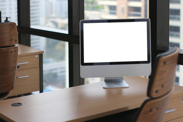 Wall Mural - selective focus at wooden table desk in office business room with big computer monitor and windows background