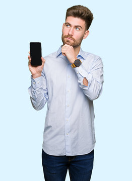 Young handsome man business showing smartphone screen serious face thinking about question, very confused idea
