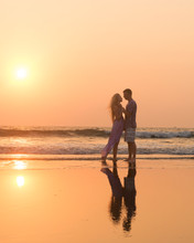 Silhouettes Of Young Couple In Love Having A Great Time On The Honeymoon Staying On The Beach With Beautiful Red Sunset On Background