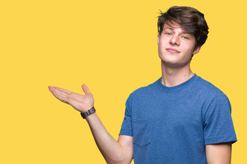 Young handsome man wearing blue t-shirt over isolated background smiling cheerful presenting and pointing with palm of hand looking at the camera.