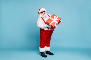 Poster - Full length photo of funny funky fat santa claus with big belly abdomen hold gift box for christmas time follow noel tradition wear red pants white gloves boots isolated over blue color background