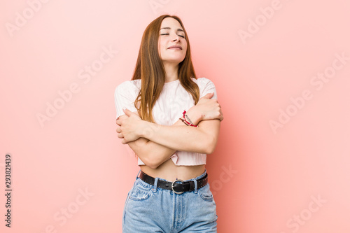 Cuadros en Lienzo Young redhead ginger woman against a pink wall hugs, smiling carefree and happy