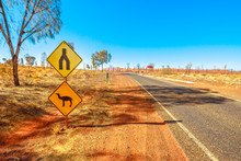 Camel Crossing Sign Warning Drive In Northern Territory, Red Centre, Central Australia. Yulara, The Village Near Popular Uluru-Kata Tjuta National Park. Australian Outback Landscape In Dry Season.