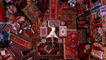 Beautiful Happy Girl In A Long White Dress Laying On The Carpet And Rugs In Goreme, Cappadocia, Turkey. Top View Drone.