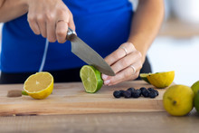 Woman's Hands While She Cutting Limes Over Wooden Table In The Kitchen.