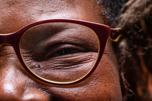 An Extreme Closeup View On The Eye Of An Elderly African Woman Wearing Reading Glasses, Jovial And Smiling Wise Old Woman In Close-up Detail.
