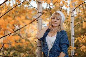 a woman with blond hair in a gray jacket and jeans, shot against the autumn foliage on a cloudy day