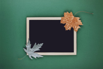 Autumn minimal flat lat, mockup, composition. Black blank frame chalk board and golden silver metallic dry maple leaves on green blue paper background