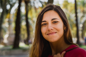 Smiling teenager looking at the camera and holding a bag on the park.