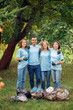 © Viktoriia - Volunteering. Young people volunteers outdoors near bags with litter hugging thumbs up smiling cheerful