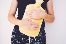 Extreme Close-up Mid Section Of A Woman Holding Yellow Hot Water Bag On Abdomen
