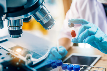 lab technician assistant analyzing a blood sample in test tube at laboratory with microscope. Medical, pharmaceutical and scientific research and development concept.