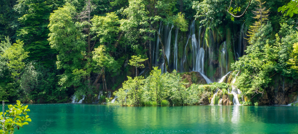 Crystal clear, pure water rushing down mossy rocks into a beautiful azure colored lake at the Plitvice Lakes National Park, Plitvička Jezera, Croatia - obrazy, fototapety, plakaty 