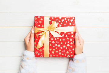 Woman hands give wrapped christmas or other holiday handmade present in colored paper . Present box, decoration of gift on white wooden table, top view with copy space