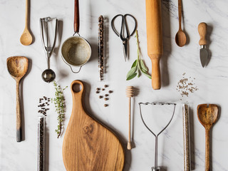 Flat lay various metal, wooden kitchen tools and dry spices in glass tube and raw herbs on a marble background. Top view.