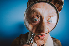 Funny Portraits With Old Grandmother. Senior Woman Acting As An Investigator With The Magnifying Lense