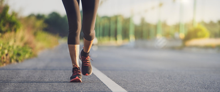 Fototapete - Runner feet running on road closeup on shoe. Woman fitness sunrise jog workout wellness concept. Young fitness woman runner athlete running at road