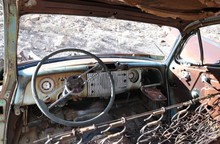 Looking Inside Interior Of Old, Ancient, Rusty, Rusted And Abandoned Car Wreck Of An Old Vintage Automobile Or Jalopy With Shredded Material And Padding On Seats, Broken Windows And Steering Wheel