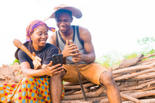 Excited African Couple Doing Internet Banking On Their Farmland. Male And Female Farmers Using Smartphone