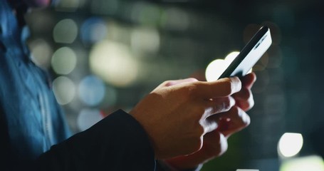 Slow motion close up of an young man hands using a smartphone phone in a center of the city by night.